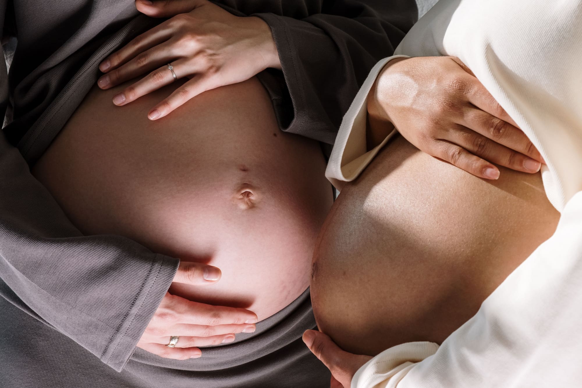 Two pregnant women gently touching their bellies, symbolizing togetherness in motherhood.