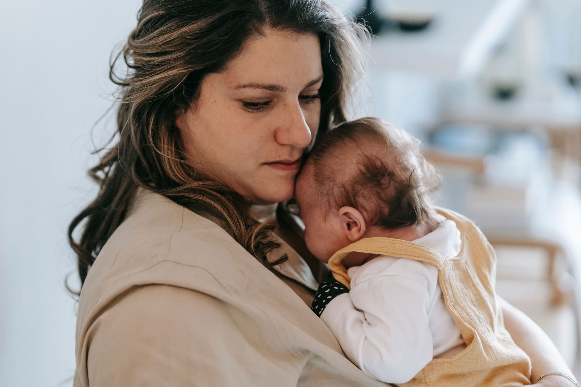 A mother gently holding her baby in a comforting embrace inside a cozy home setting.